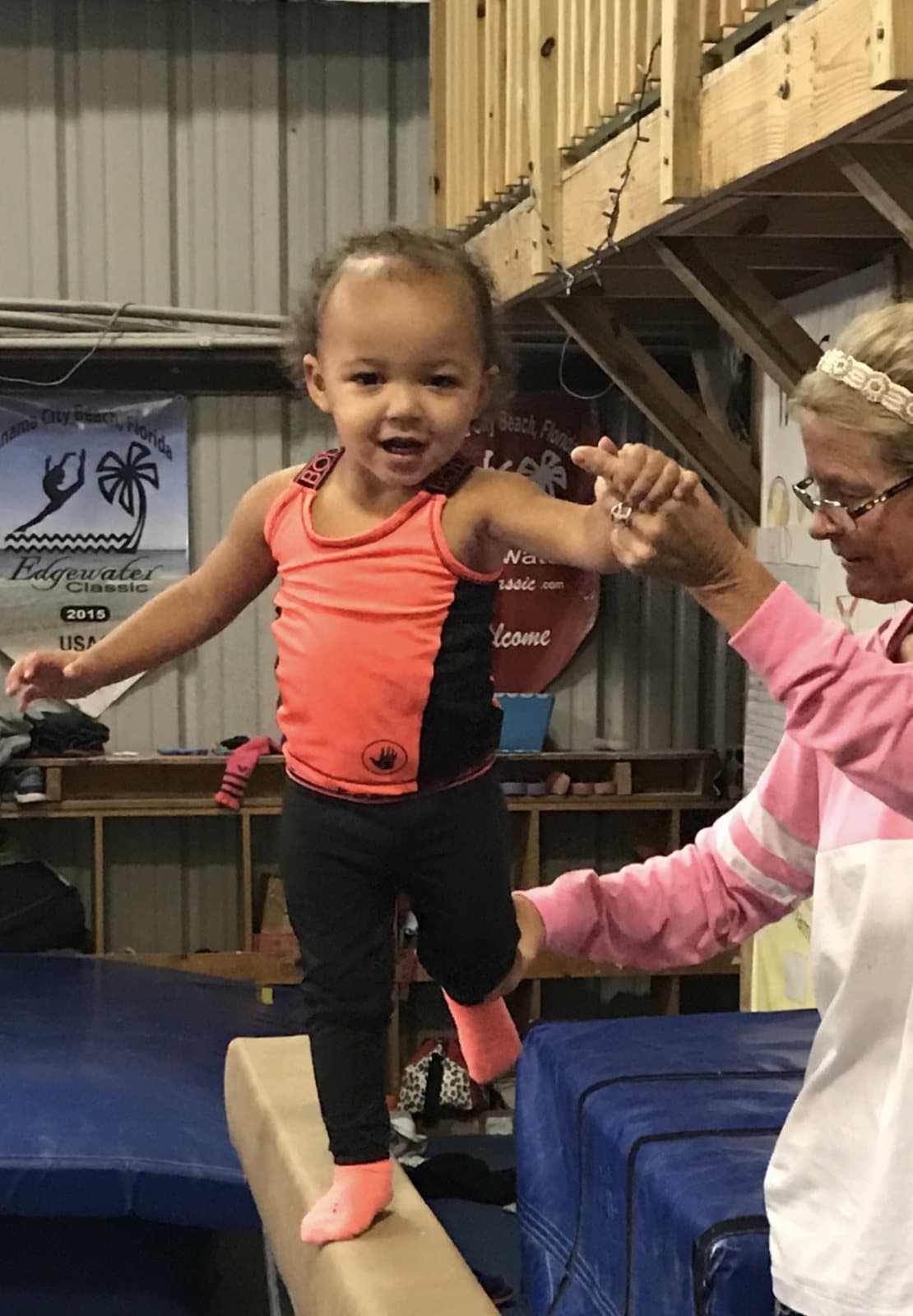 An Edgewater coach holding a little gymnast's hand as she walks the beam